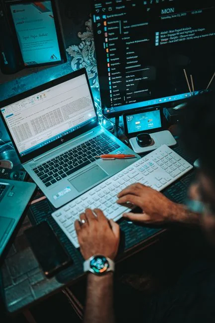 Hands typing on a laptop with cryptocurrency charts and smartphone display in view, focusing on digital finance.